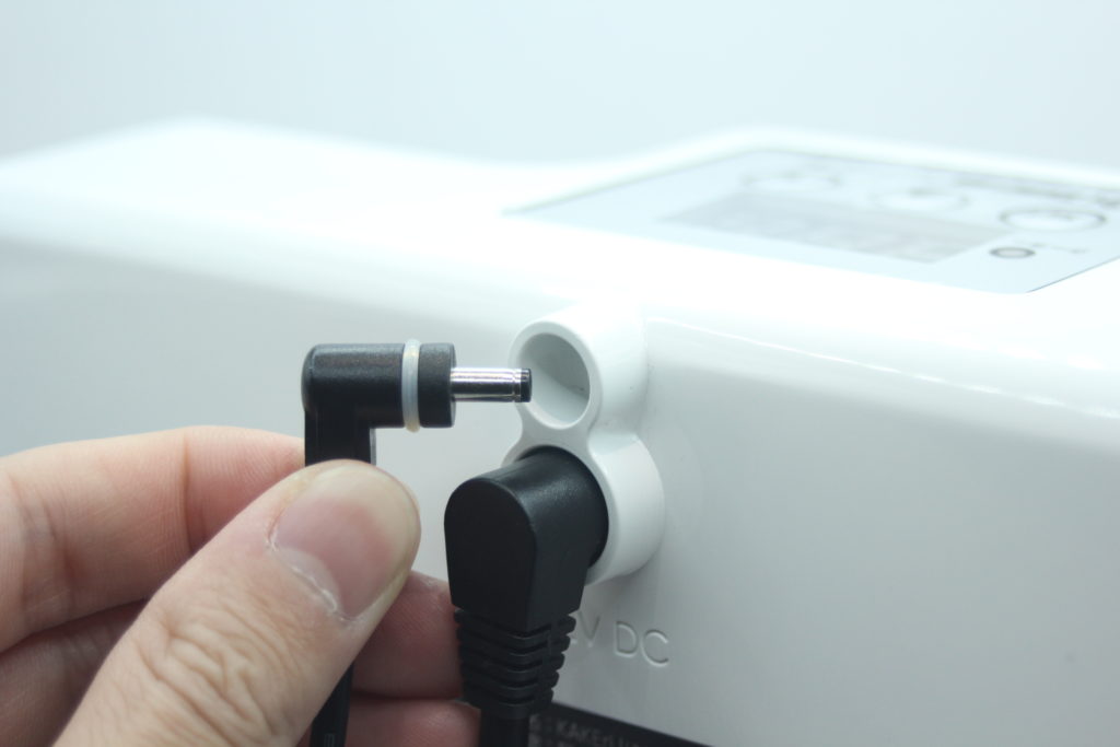 白い機器の電源ポートにDCプラグを差し込む手元
