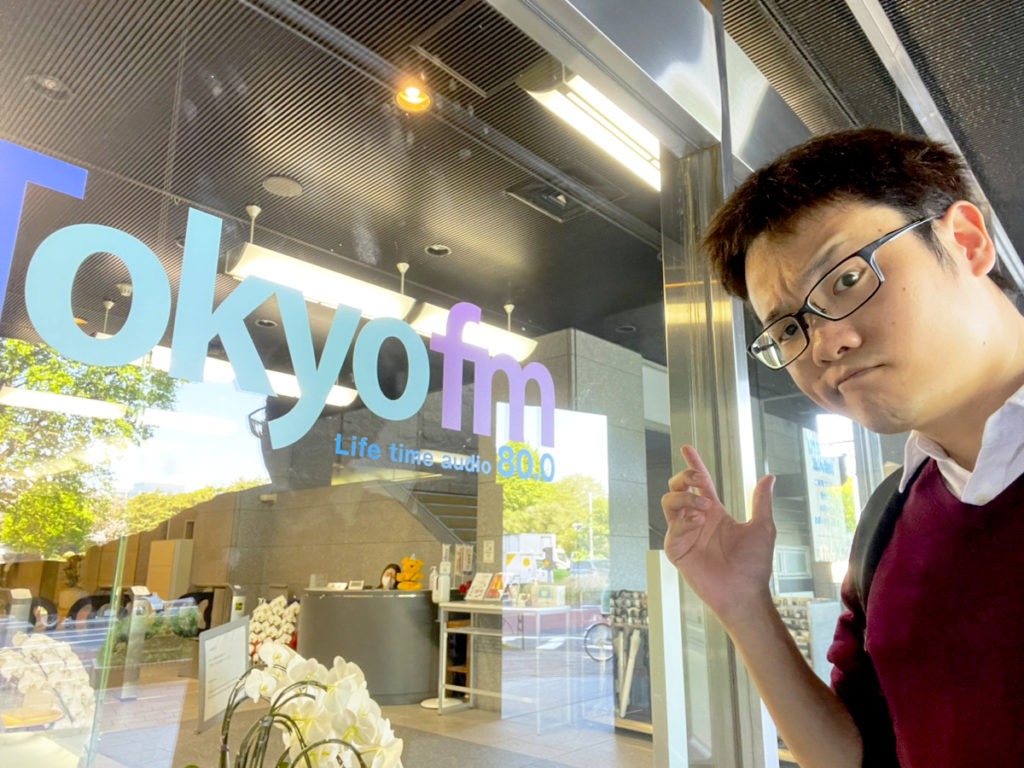 TOKYO FMのロゴがある入口前に立つ眼鏡の男性