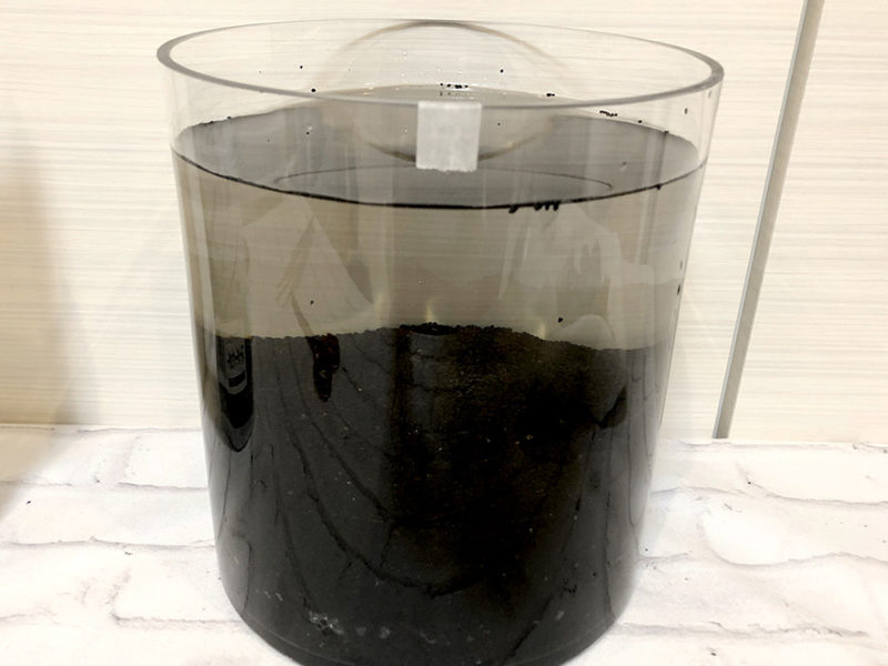 円柱容器に入った黒いソイルと濁った飼育水