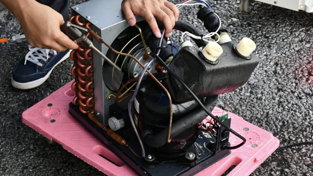 屋外で水槽用クーラーの内部を点検する人の手元