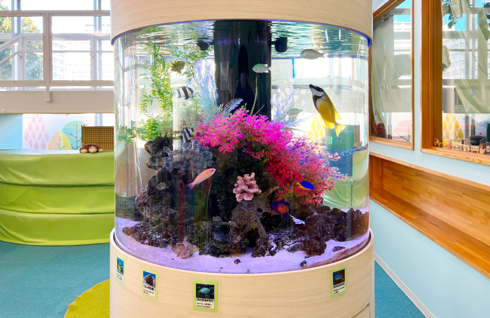 ピンクの人工水草と海水魚が泳ぐ円柱型水槽の設置事例