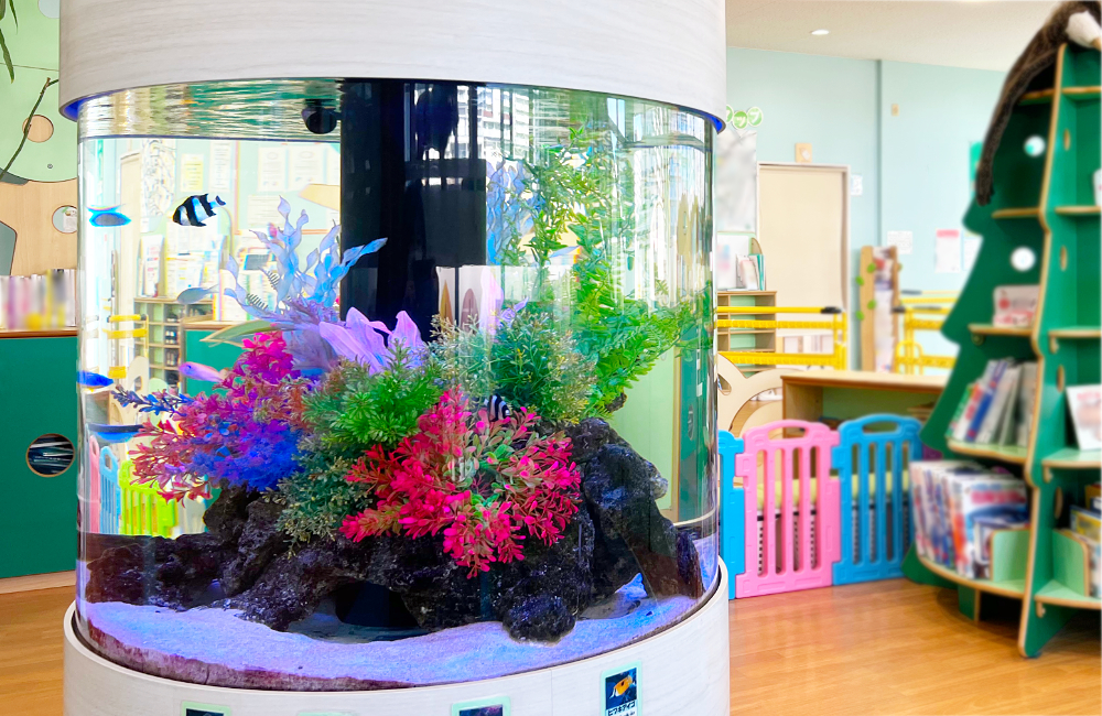 カラフルな人工水草と熱帯魚が泳ぐ円柱型水槽