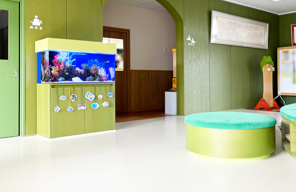 緑の壁の部屋に設置された海水魚水槽と丸いスツール